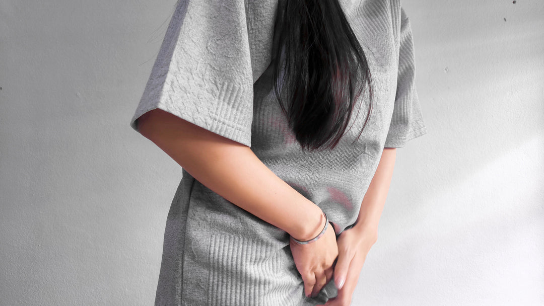 Asian woman holds hands protectively over painful pubic area 