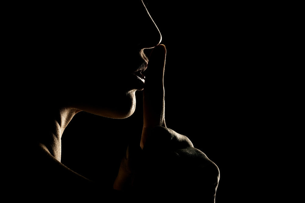 Mysterious backlit woman holds finger to lips to keep a secret