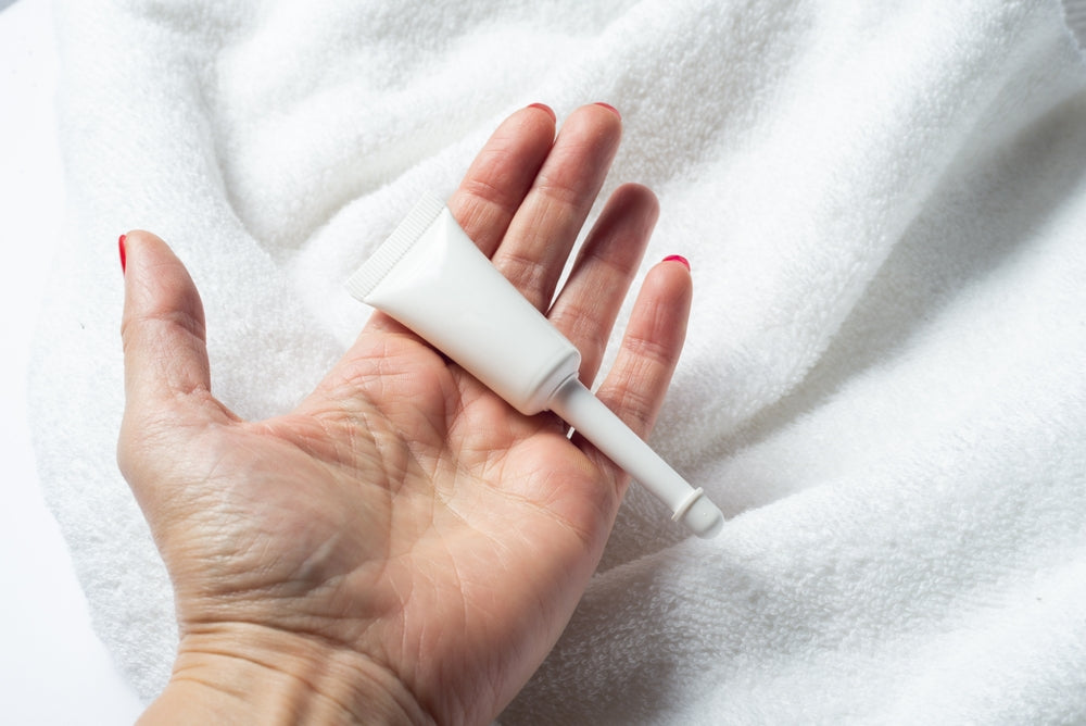 White woman holds unlabeled vaginal cream applicator on white background